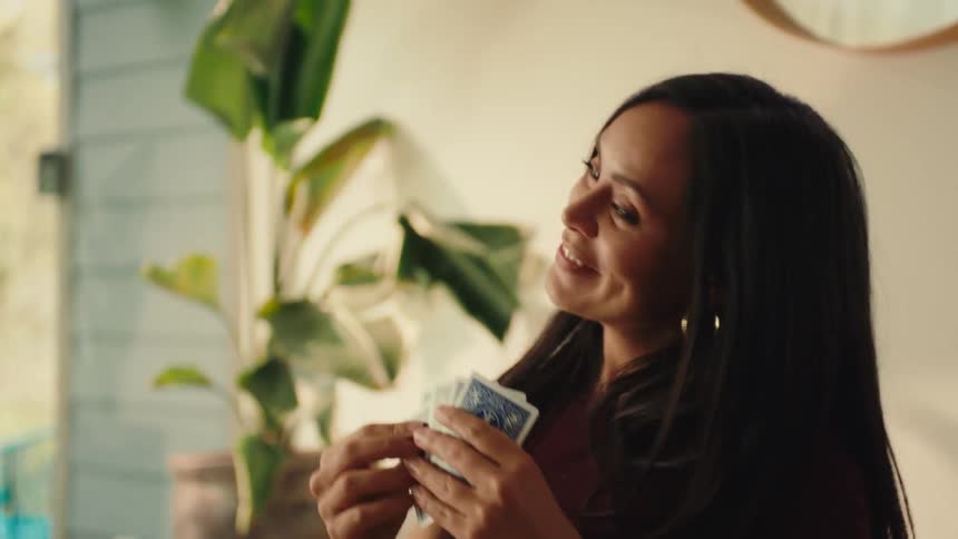 A confident woman smirks while holding playing cards suggesting shes winning a game in a relaxed indoor setting