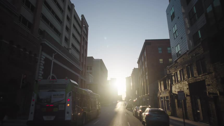 A city bus travels down an urban street at sunrise