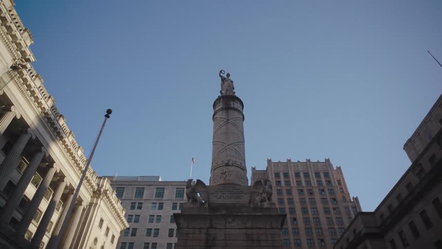 A lowangle shot of a historic monument with statues framed by surrounding classical buildings against a clear blue sky