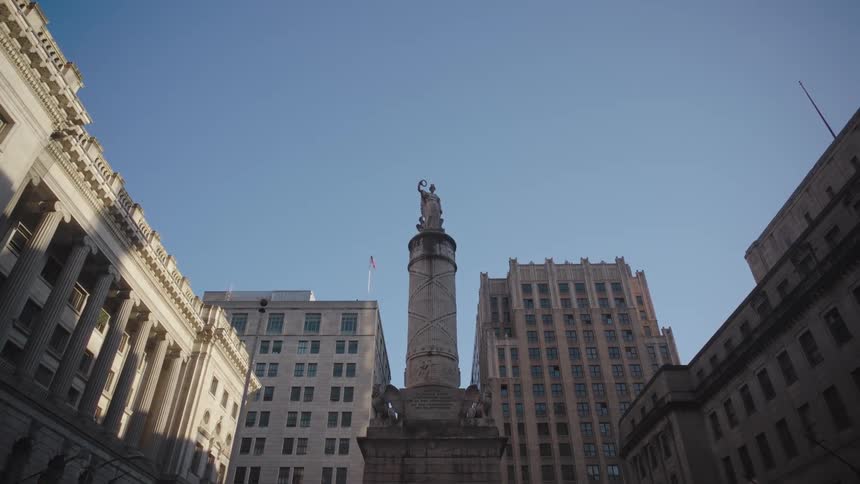 A circular monument with a statue on top in the middle of a square surrounded by buildings
