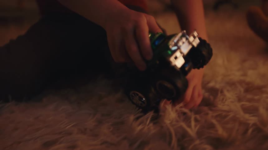 Child rolling toy monster truck across white shaggy carpet