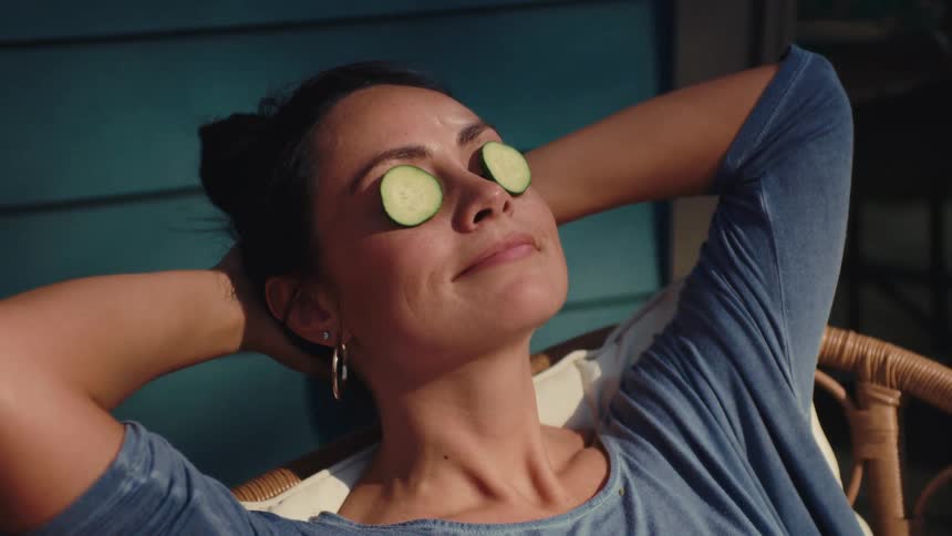 Smiling woman relaxing outdoors with arms behind her head and cucumbers over her eyes