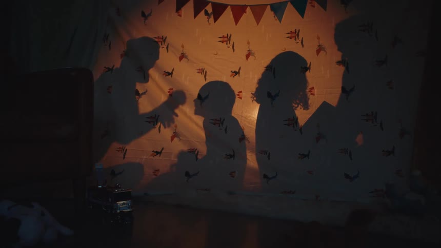 Family sitting on the floor behind a sheet interact happily while silhouetted by a light