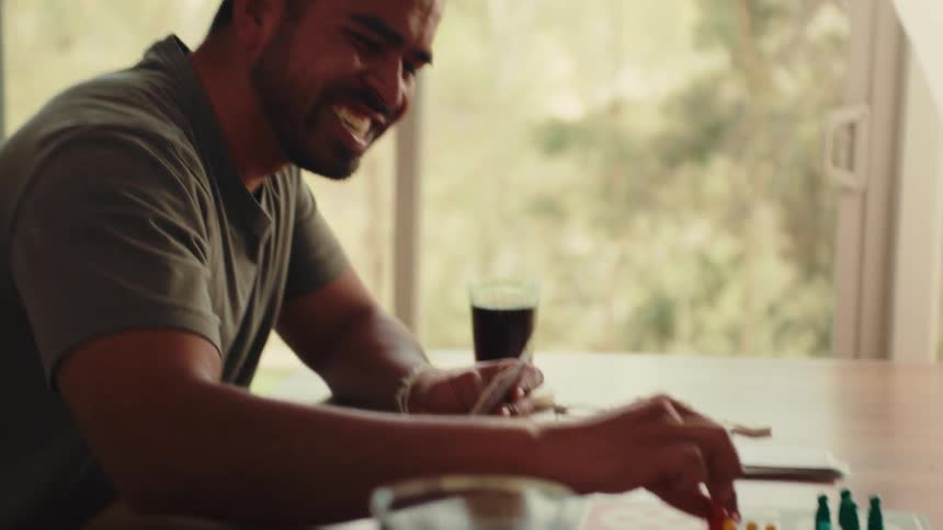 A man joyfully plays a board game at a table near a window enjoying a relaxed moment in a cozy home setting