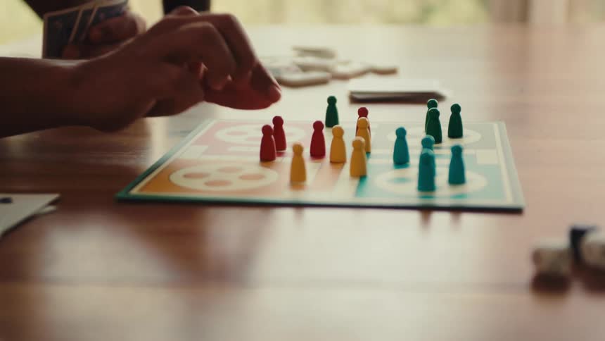 A human hand using a board piece to play a game that is on a table
