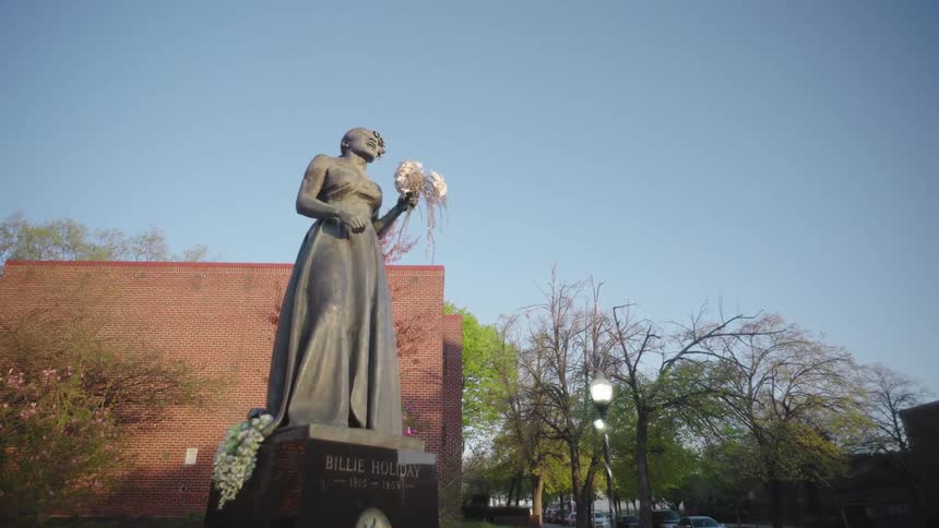 A statue of a woman is positioned in front of several buildings