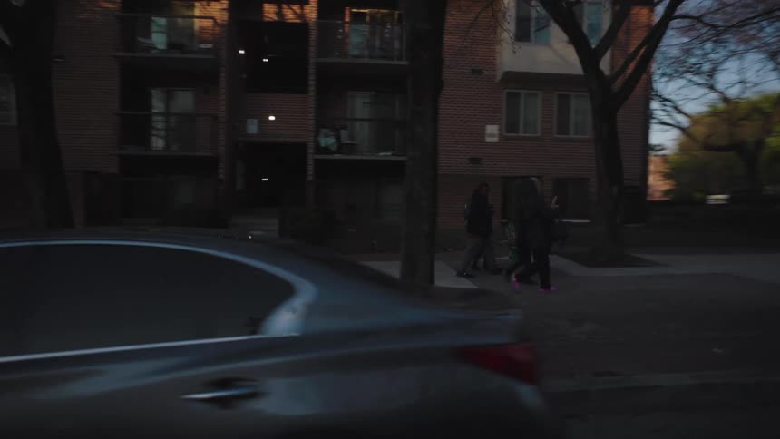 People are walking on the sidewalk past the apartments