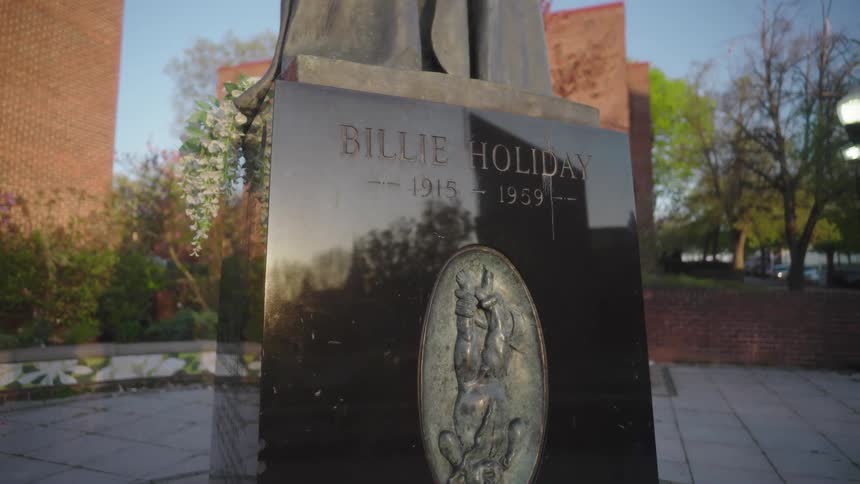A statue honoring jazz singer billie holiday stands in a public plaza with her name and dates engraved on a dark pedestal