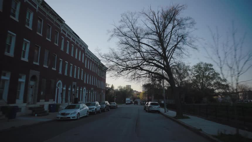 Vehicles line a road in a residential neighborhood at dusk