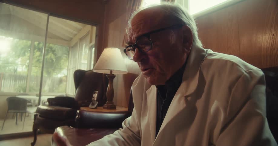 Elderly man sitting in living room wearing white blazer and talking in front of a laptop