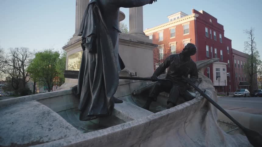 A sculpture of a boat and two men one sitting and rowing the other standing and giving orders