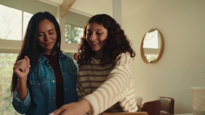 An adult woman and a teenage girl in the kitchen at midday working together to prepare dough