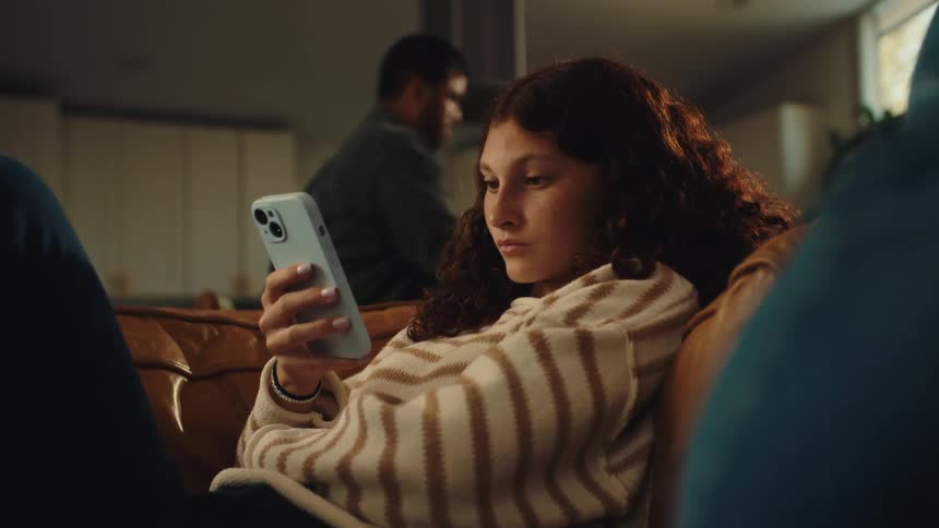 The face of a redhaired teenage girl who is using her cell phone while sitting on the sofa