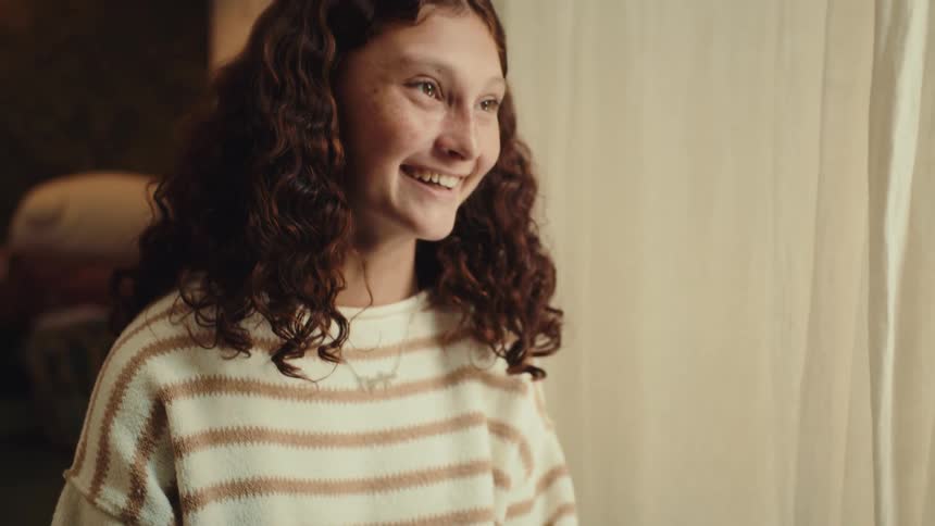 A teen girl in a striped sweater is carefully painting the fingernails of another persons outstretched hand