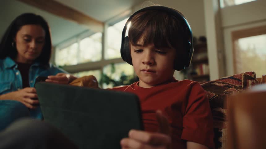 A boy and girl use electronics devices while sitting on a sofa