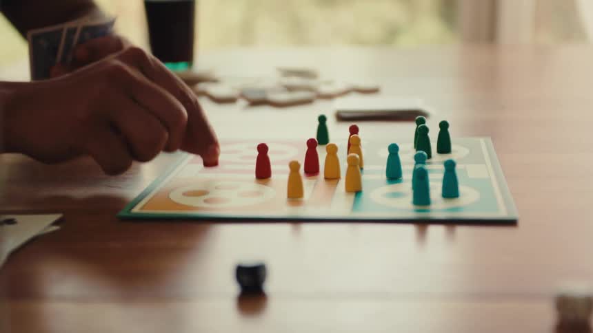 Hand throwing dice on a table and moving pegs in a board game