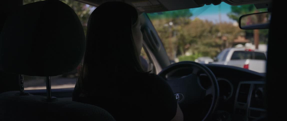 The face of a woman who is turning a steering wheel driving a car while looking forward