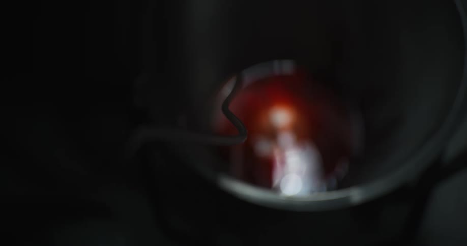 Metal container contains reddish liquid with light reflection and immersed object