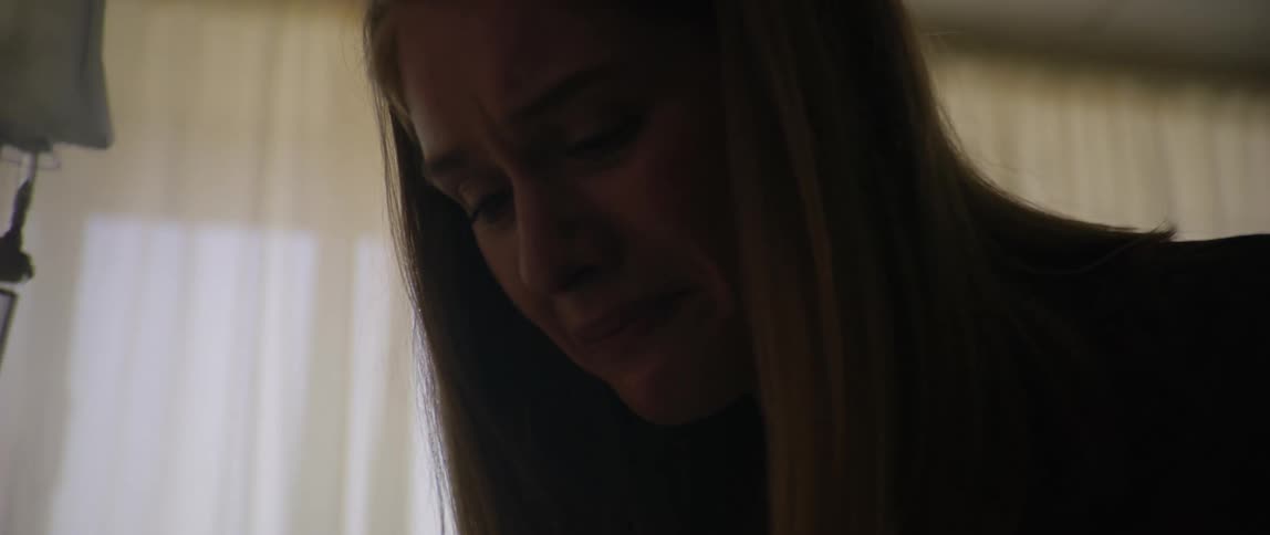 A visitor in the hospital becomes upset and beings crying as she leans towards the patient