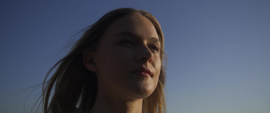 Closeup face of a lady opening her eyes while the wind blows her hair at sunset