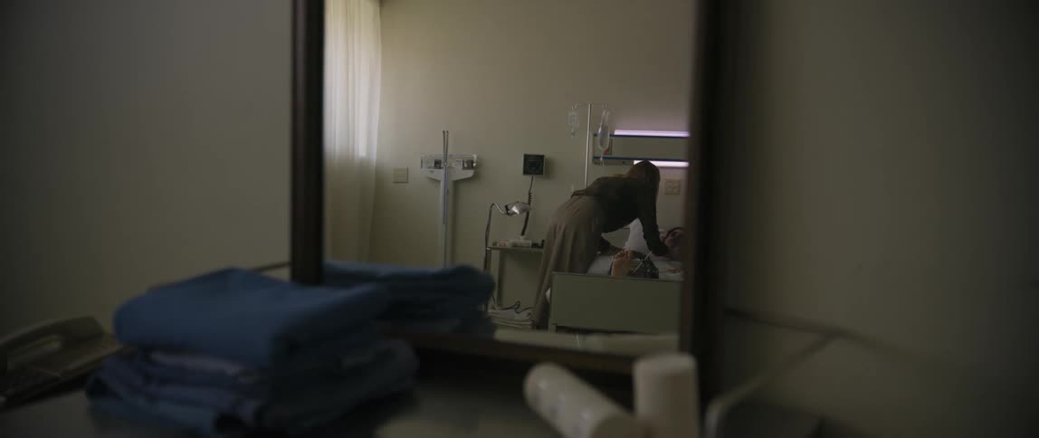 Lady walks in the hospital room and hugs a man on the hospital bed at daytime