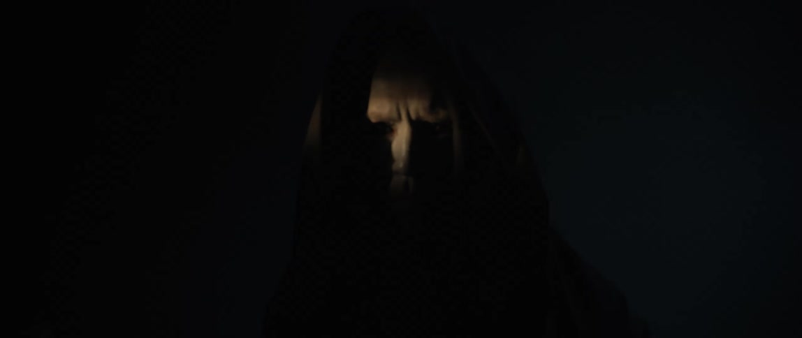 Creepy man with pure black eyes wearing a black hooded robe standing in the darkness