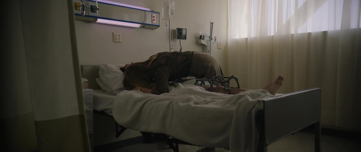 A woman leans over and hugs a sick man in the hospital bed