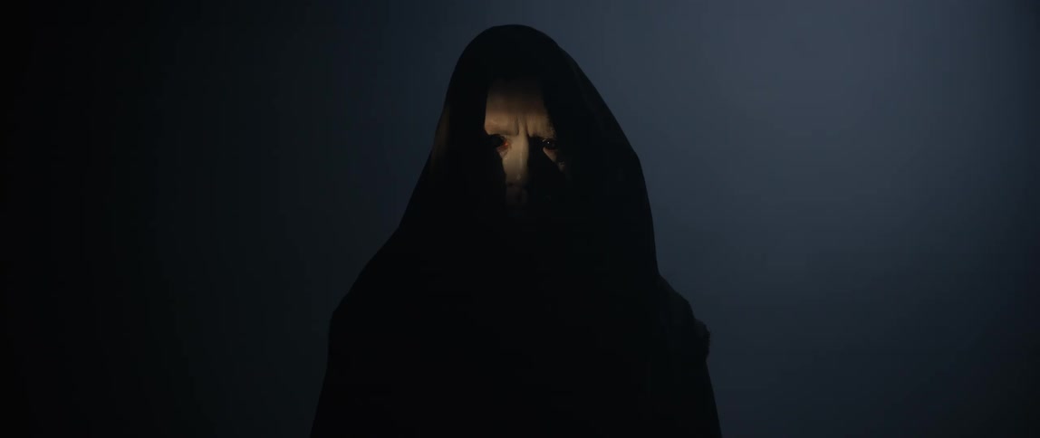Creepy man with pure black eyes wearing a black hooded robe standing in the smoke filled darkness