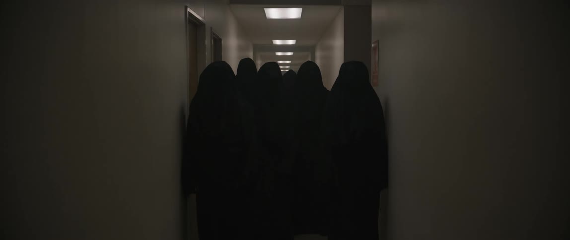 A groups of nuns stand in a dark hallway that gets illuminated by ceiling lights