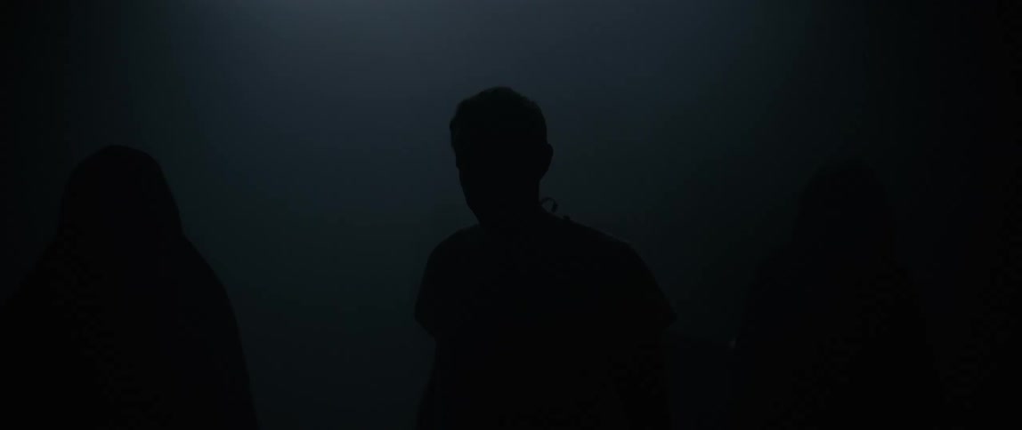 Two people in black robes lead a man through the dense fog