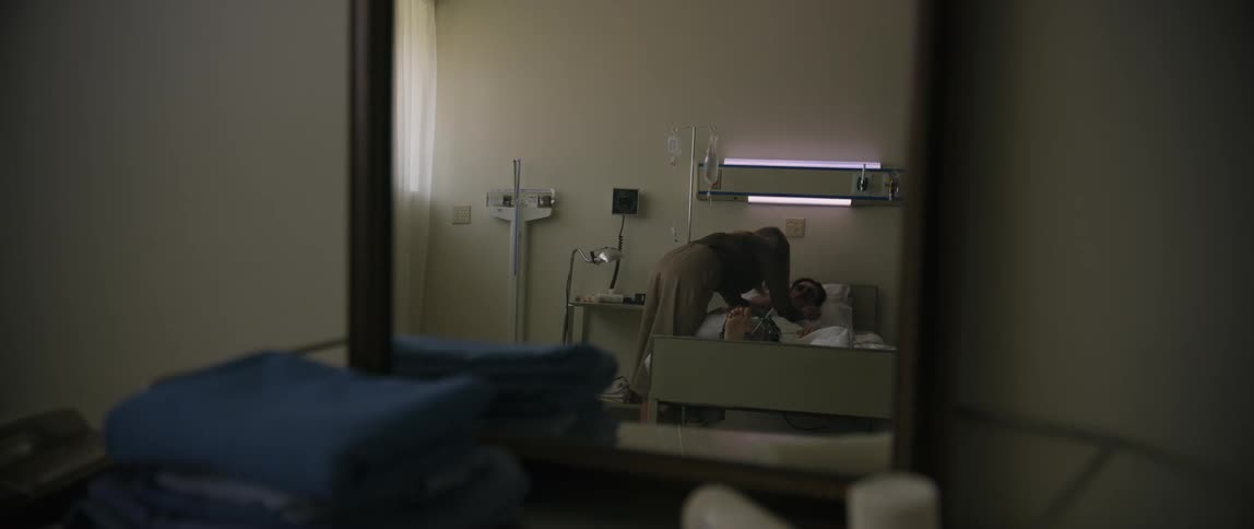 A woman is entering a hospital room and hugs a patient on the bed