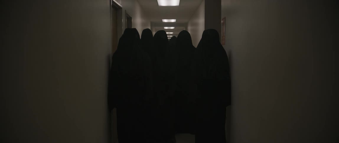 A group of hooded cloaked figures stands ominously in a dimly lit hallway creating a dark mysterious and eerie atmosphere