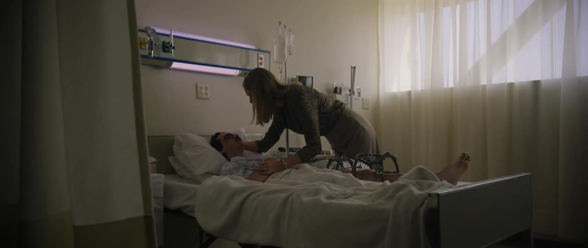 A woman enter the room and touches and hugs the male patient lying on the bed
