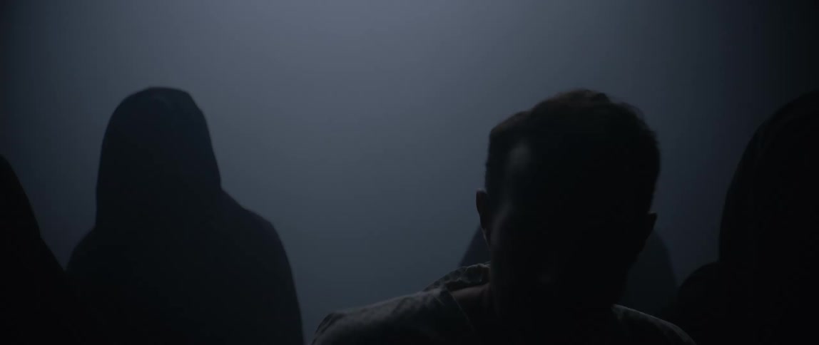 Man being escorted by a group of hooded people in a dark room
