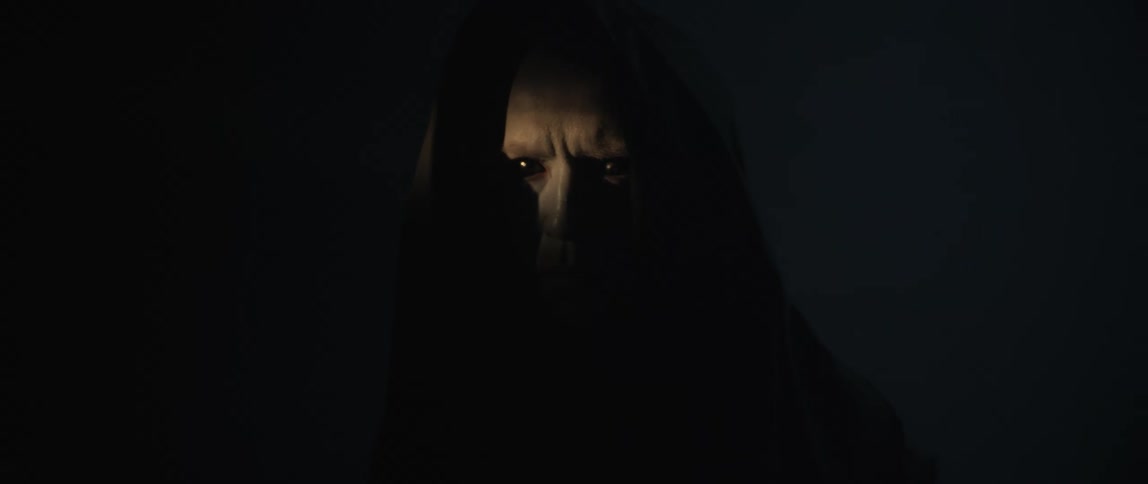 Creepy man with pure black eyes wearing a black hooded robe standing in the darkness