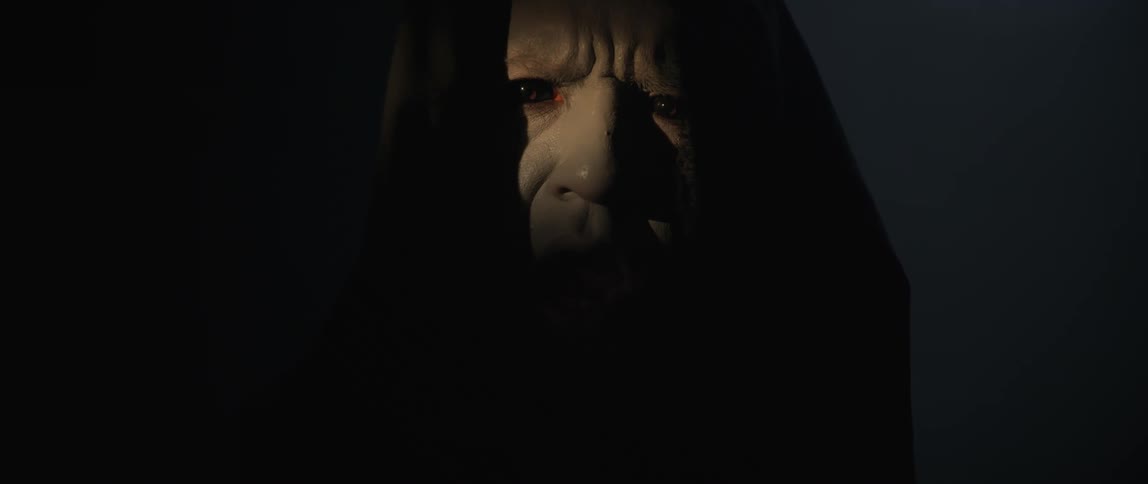 A man in black robes scowls in the dark