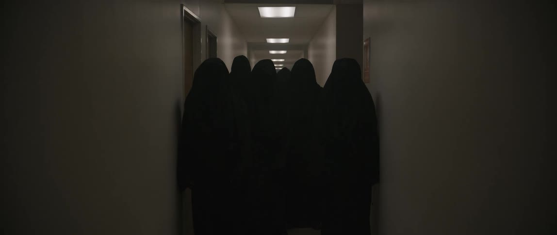 A group of people in dark robes slowly move down the hall