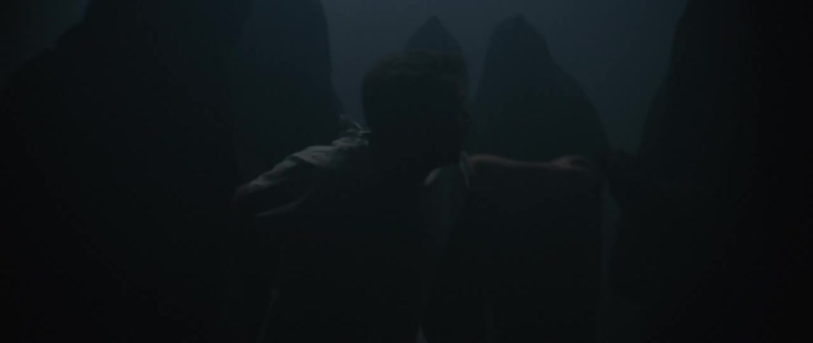 Cloaked figures crowd and seize a man in a dark foggy area