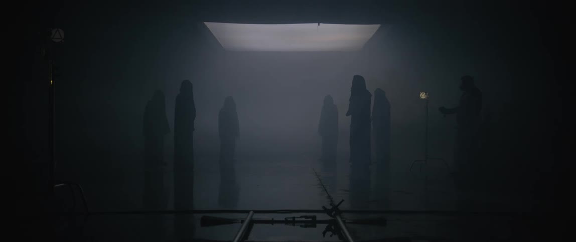 A group of figures dressed in black stand in a circle in the middle of a corridor