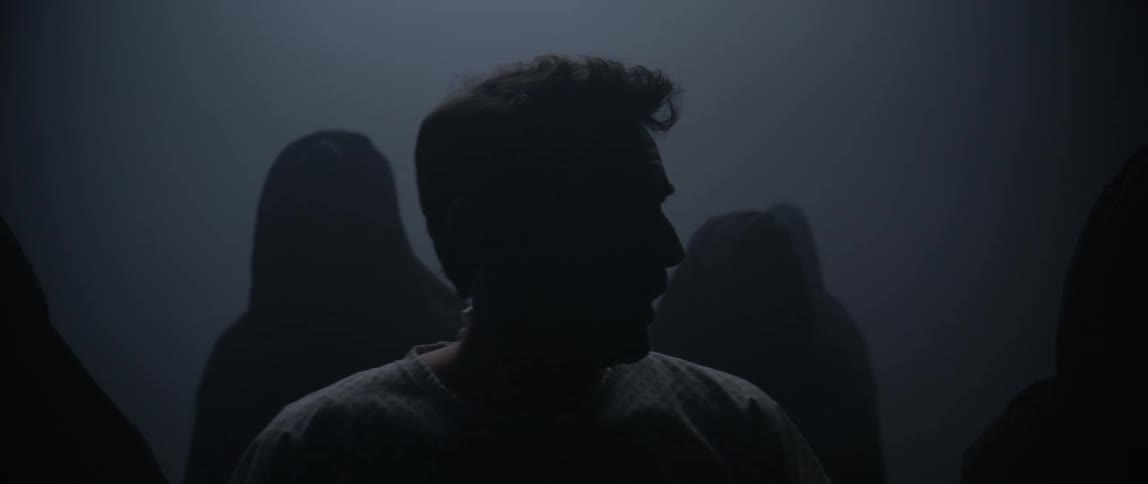 A man limps as he walks in front of a group of dark figures