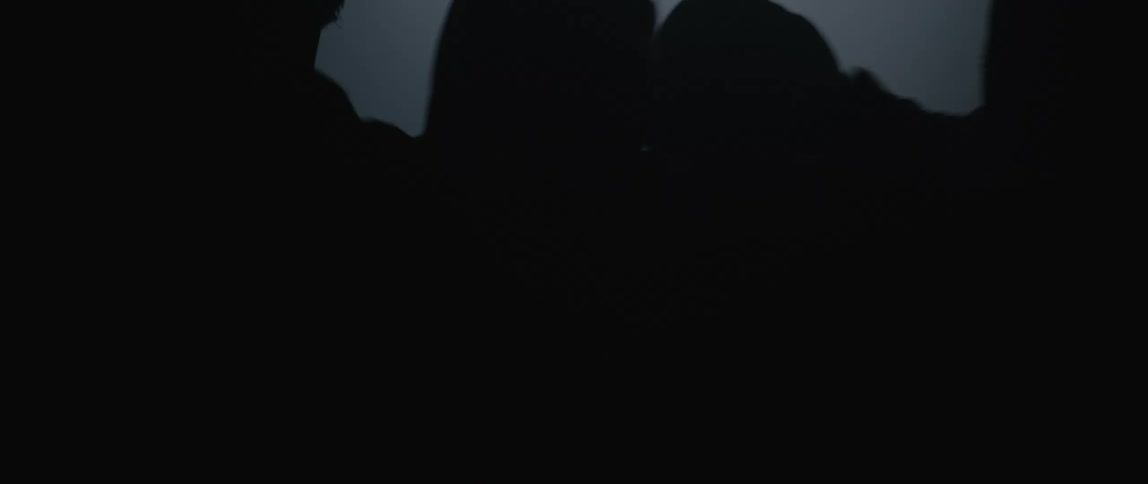 Man being restrained by several hooded people in a dark room