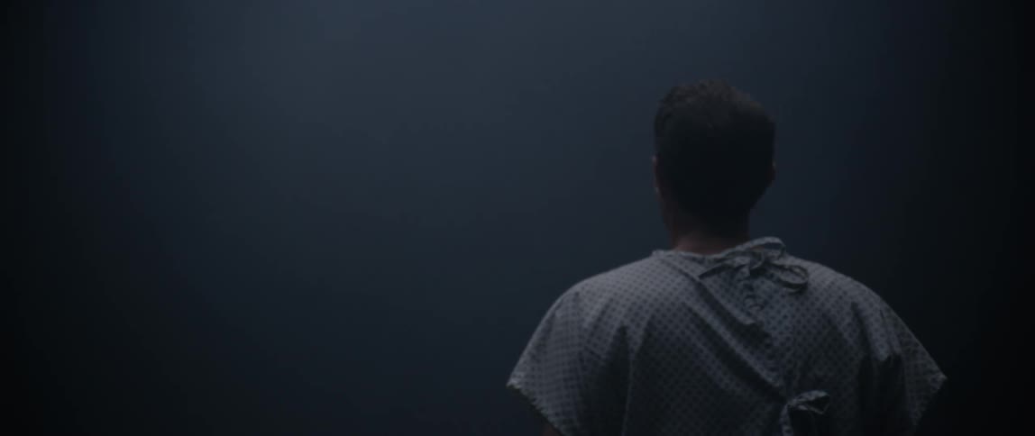 Male patient wearing a hospital gown looks around while walking through a dense fog