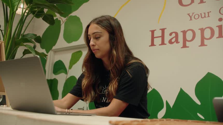 A woman works intently on her laptop at a counter in a plantthemed indoor space