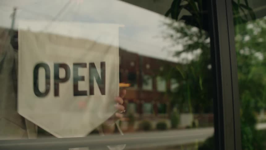 A woman closes a door and turns the door sign to say open