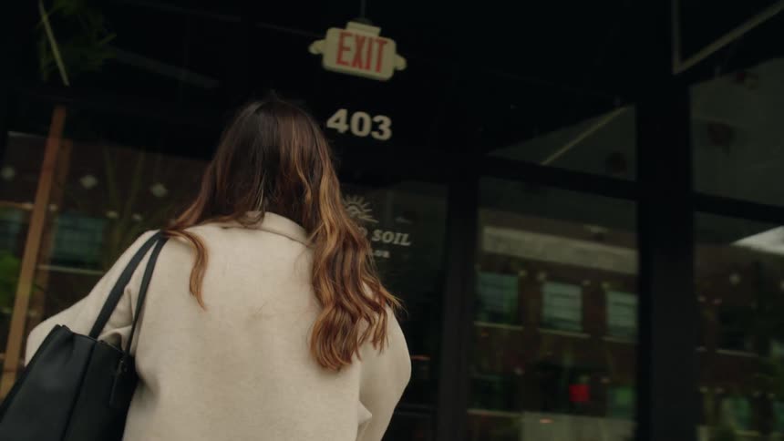 A woman with long hair and carrying a black handbag is entering a nursery
