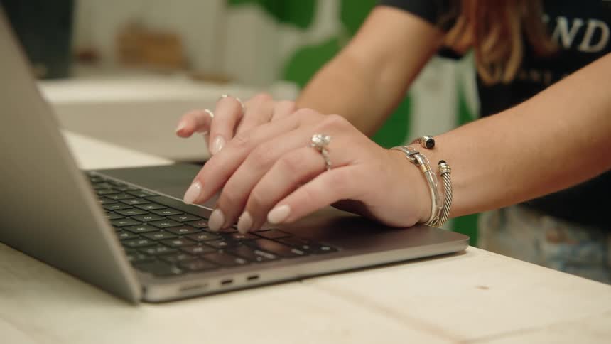A woman types on a laptop placed on a table