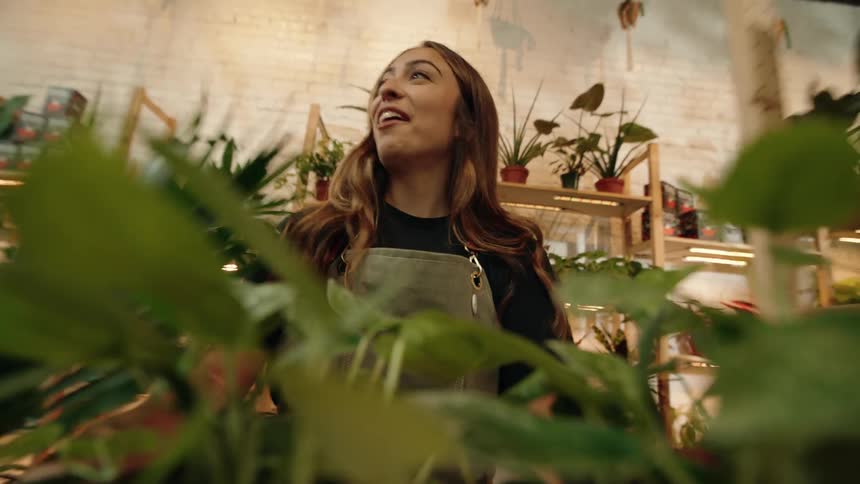 Cheerful woman with a shopping cart carrying green plants in a store