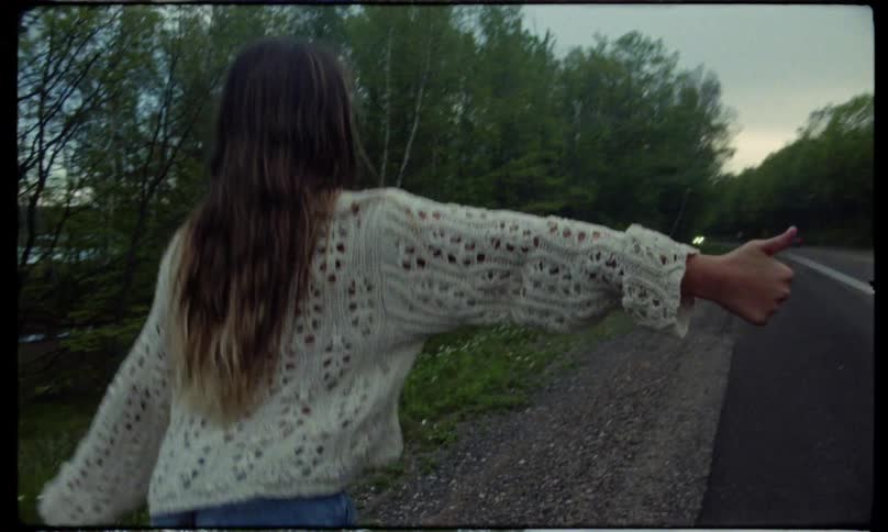 Young girl hitchhiking on side of road in the forest