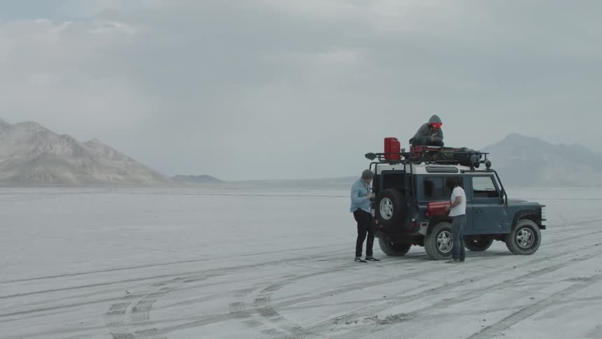 Three people stand beside a jeep style vehicle in the middle of an artic ice terrain