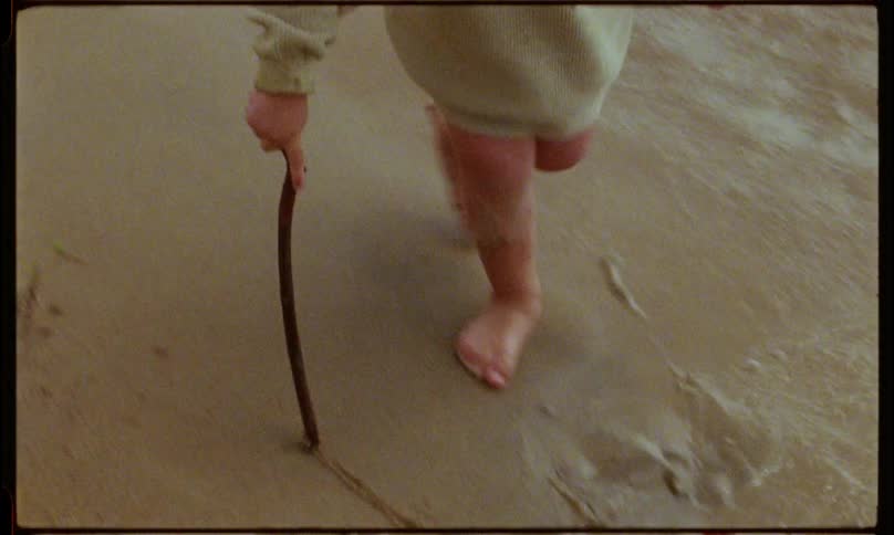 A girl child make markings on the beach sand at sunset